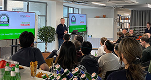 Photo of Paul Cowell, Director of Simply Rhino, standing in front of a group of seated people. Paul is introducing the upcoming Grasshopper UK User Meeting the opening slide of which is shown on two screens either side of him.